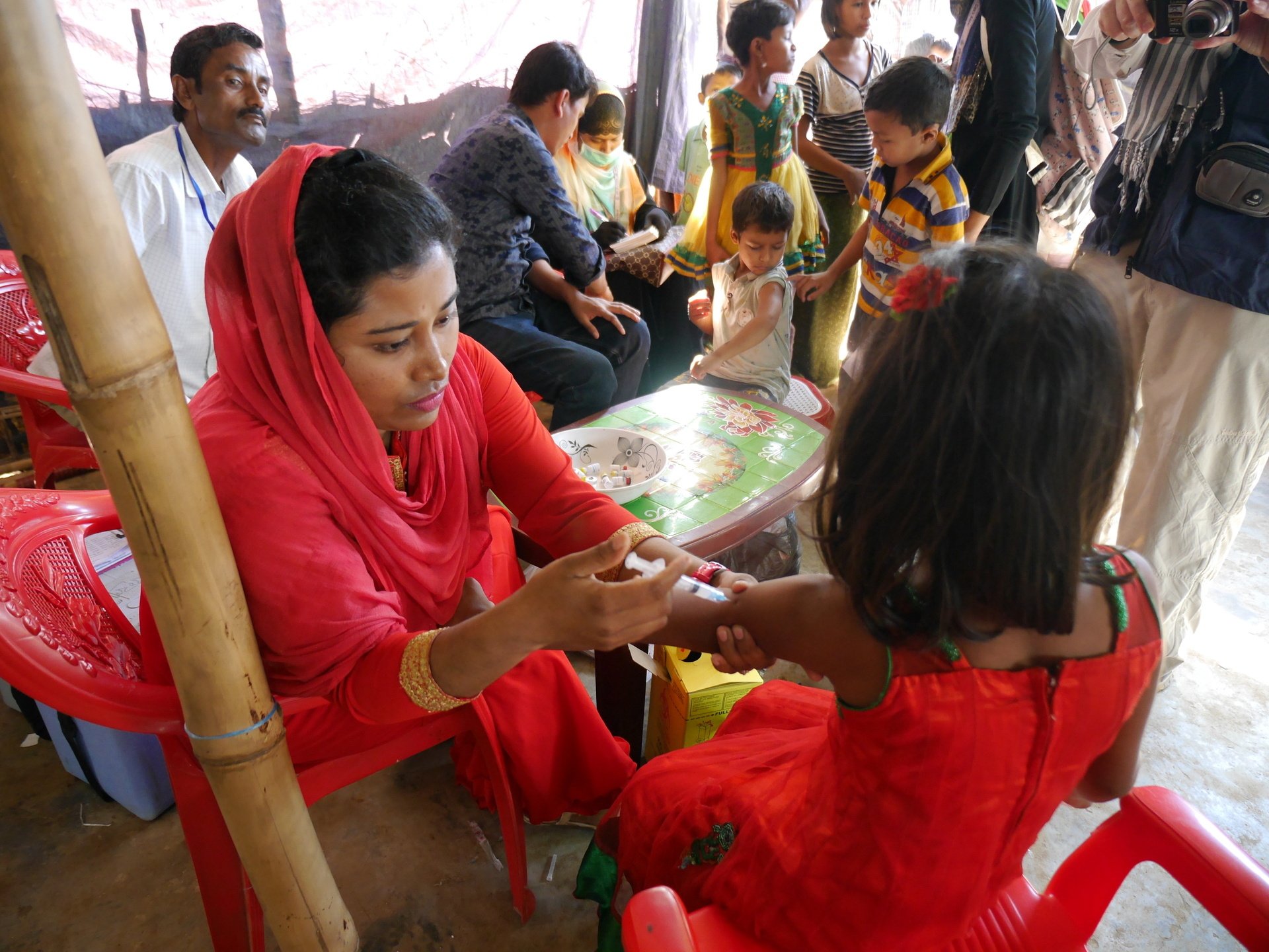 A young girl receives routine immunization as other children wait in line with their families.
